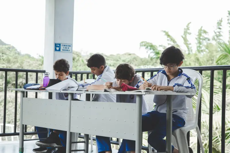Cuatro estudiantes de bachillerato del Colegio Anglo Español trabajando con sus guías en la mesa del corredor